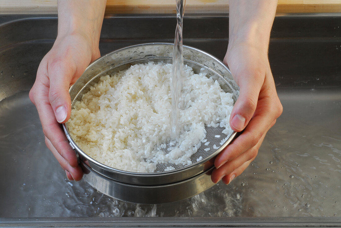 Rice being washed under running water for preparation of sushi, step 1