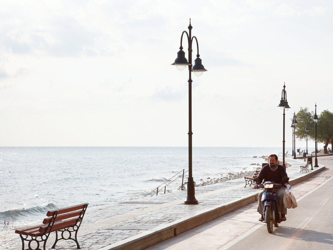 Man riding motorcycle on road across sea in Eastern Magnesia, Greece