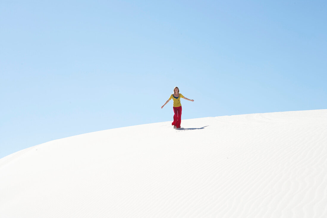 Woman in casual outfit walking on sand dune in desert