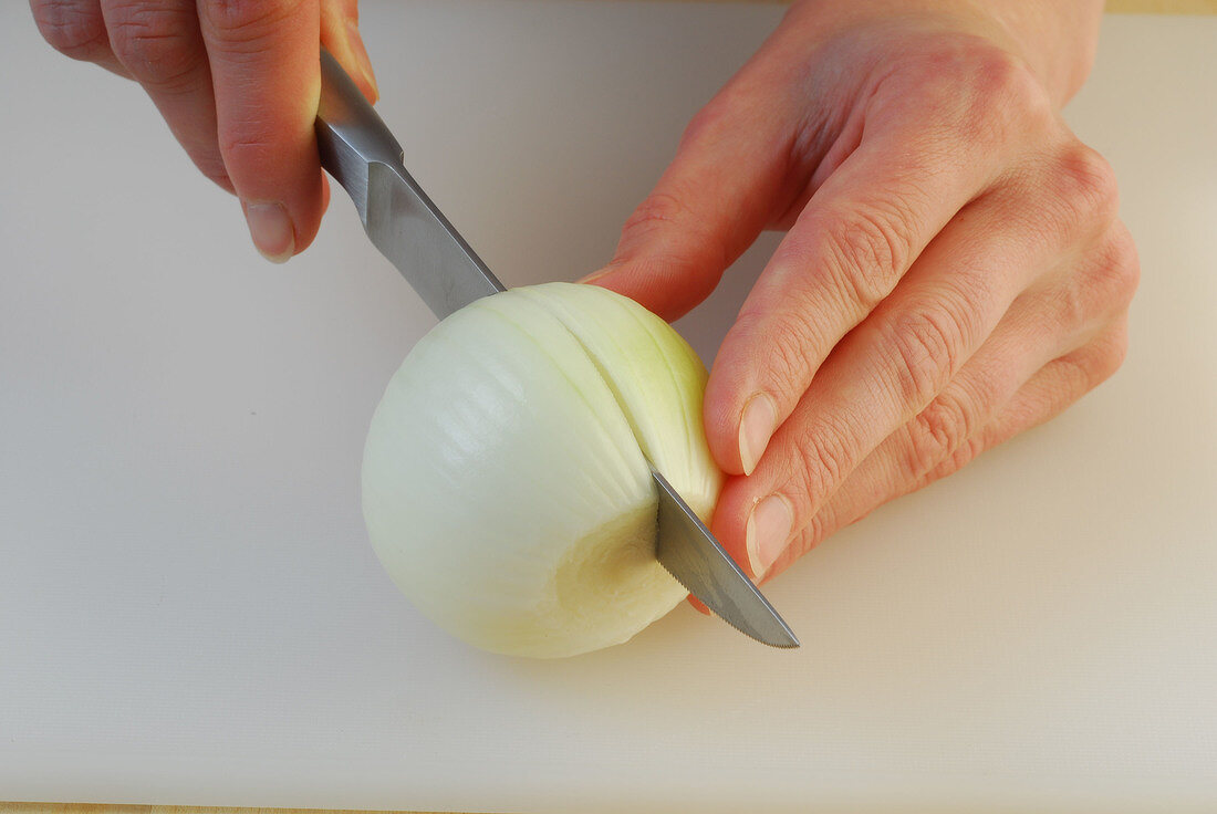 Onion being halved with knife while preparing gazpacho, step 1