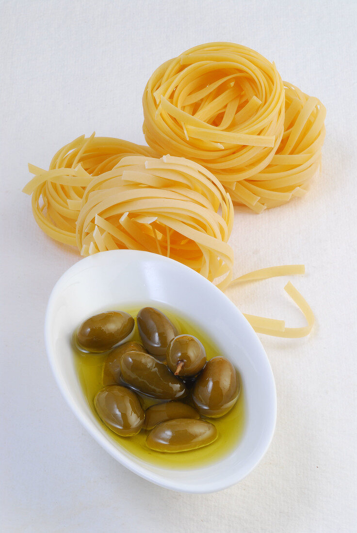 Bowl of raw olives and noodles on white background