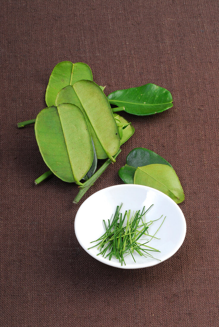 Lemon leaves on brown background and lemon grass on saucer