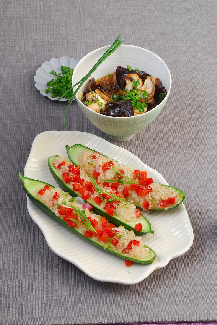 Bowl of braised mushroom and cucumbers stuffed with rice and peppers on plate