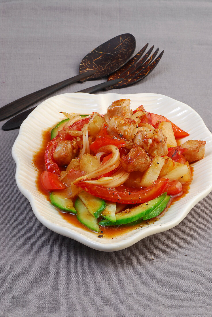 Sweet and sour pork with pineapple, bell pepper, cucumber and tomato in serving dish
