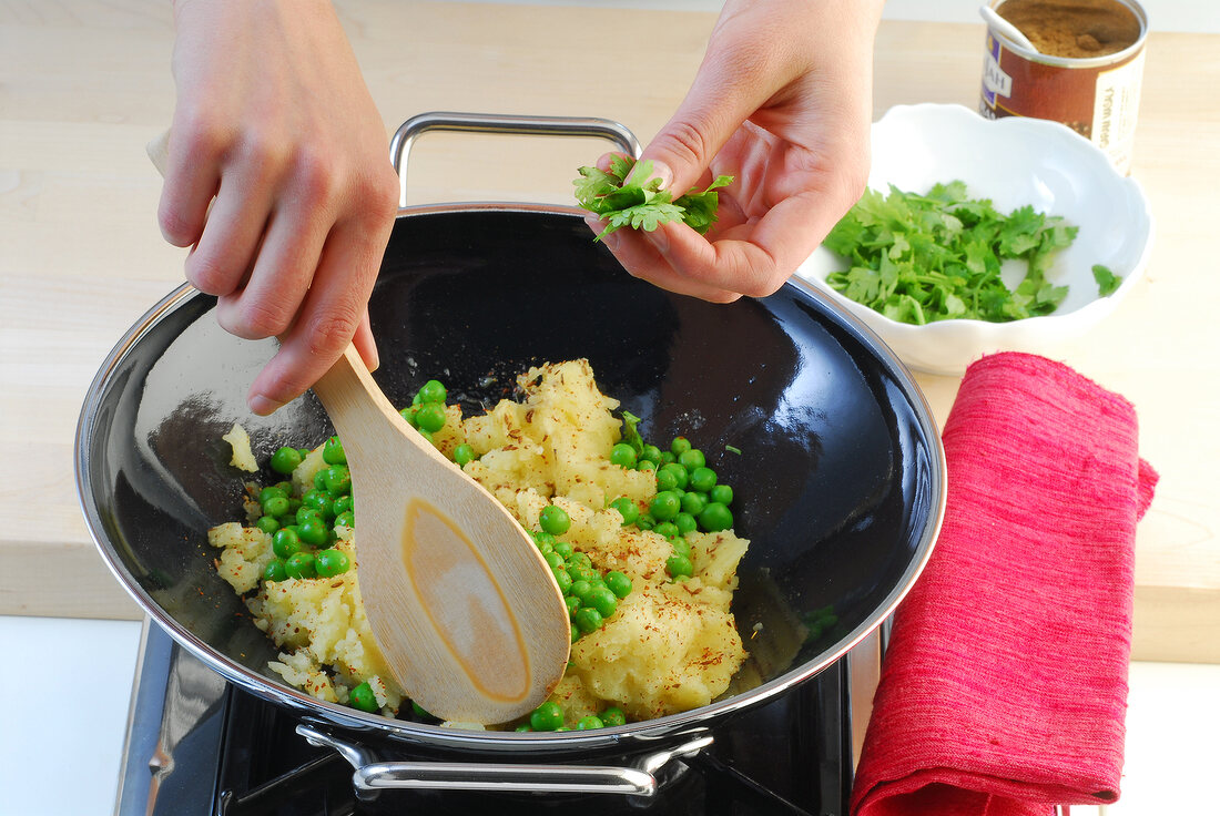 Mashed potatoes, peas and coriander being fried in wok while preparing samosas, step 2