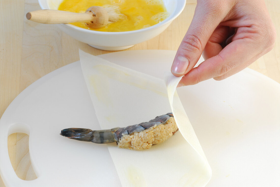 Stuffed shrimp being wrapped in dough sheet while preparing crunchy prawns, step 2