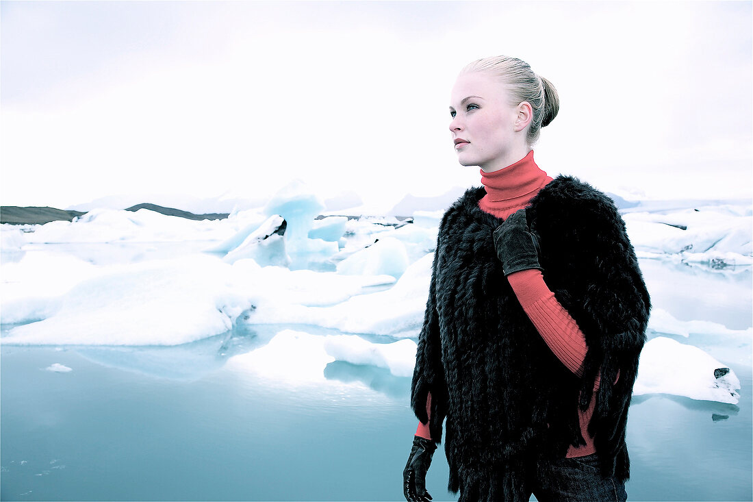 Contemplative blonde woman wearing fur poncho standing near floes and looking away