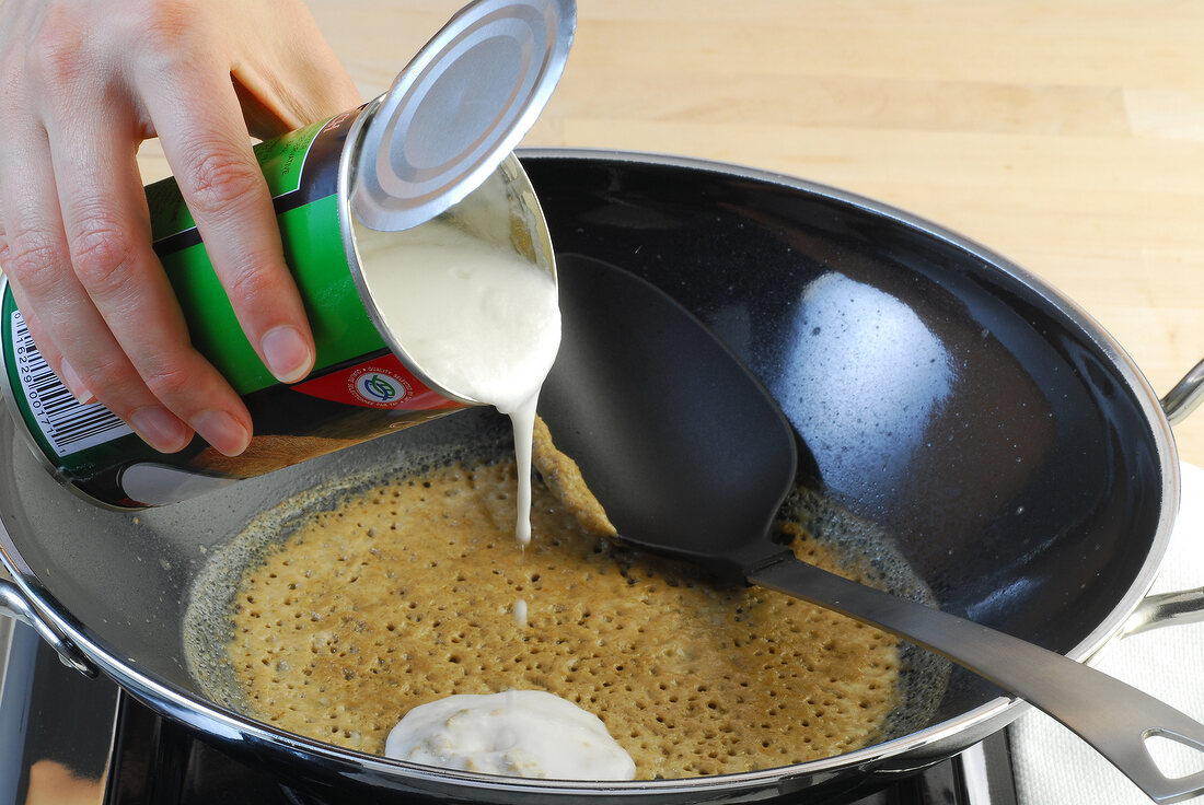 Coconut cream being added to curry paste in wok while preparing green curry, step 1