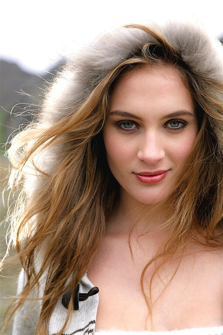 Beautiful gray eyed woman with long windswept hair wearing fur lined hood, smiling