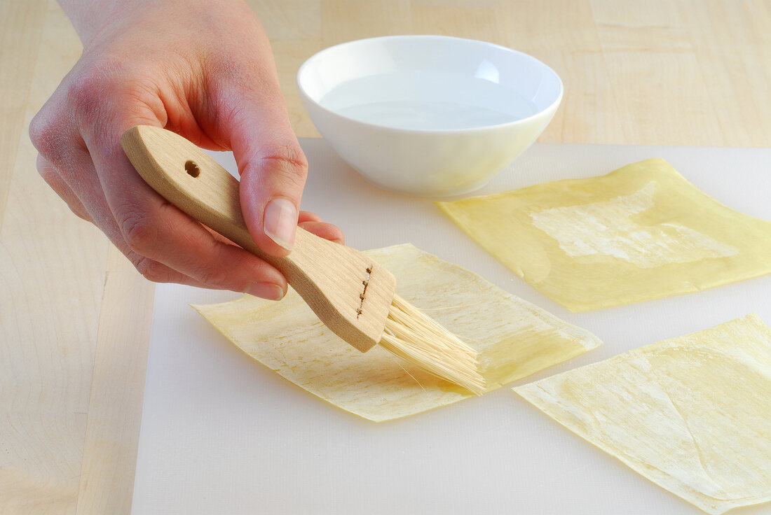 Edges of dough sheet being brushed with water while preparing wontons, Step 2