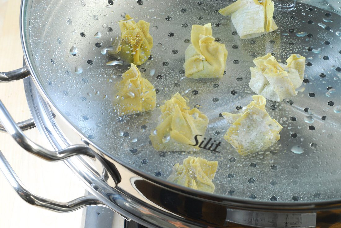 Stuffed dough being steamed in steamer while preparing wontons, step 5