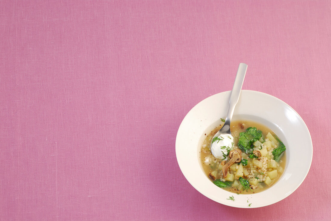 Bowl of barley soup with spinach and spoon