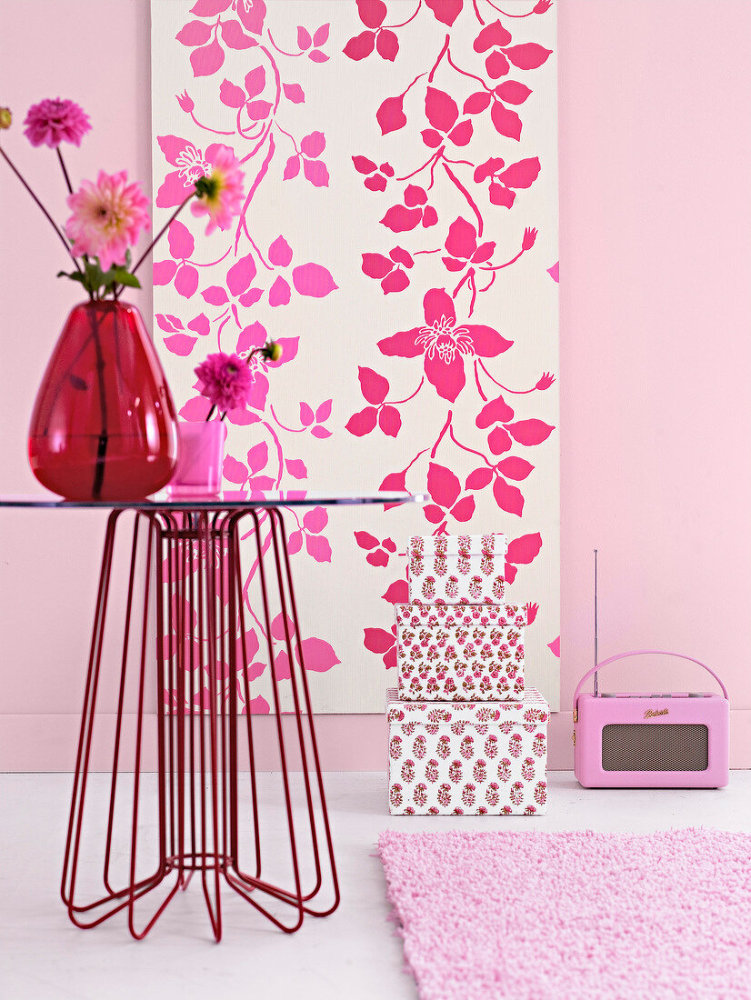 Table with red and pink flower vase against MDF board with pink floral pattern wallpaper