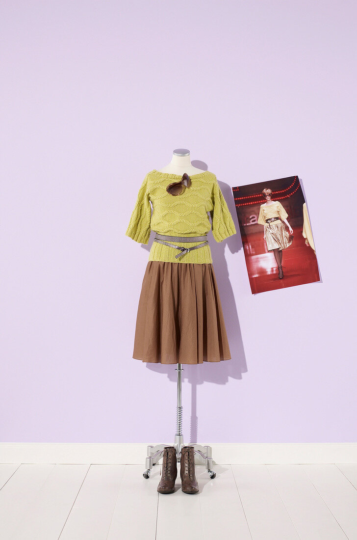 Green knit sweater, brown skirt, belts and sunglasses displayed on dressmakers model