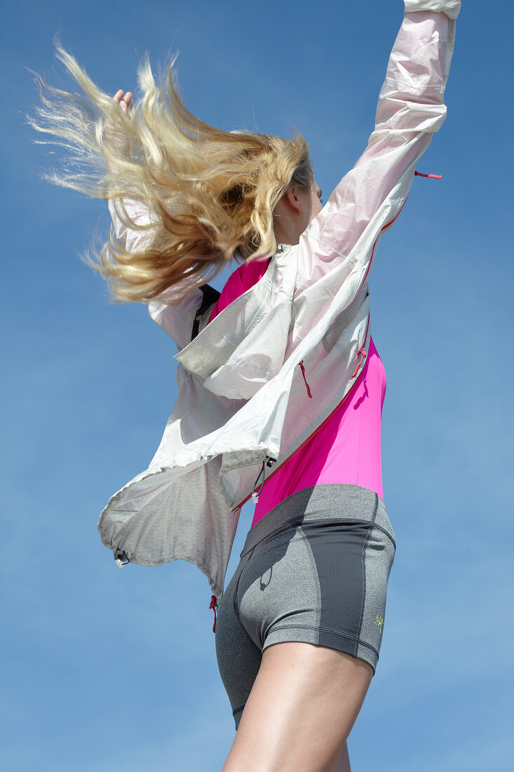 Side view of woman with windswept hair wearing jacket and shorts raising her arms
