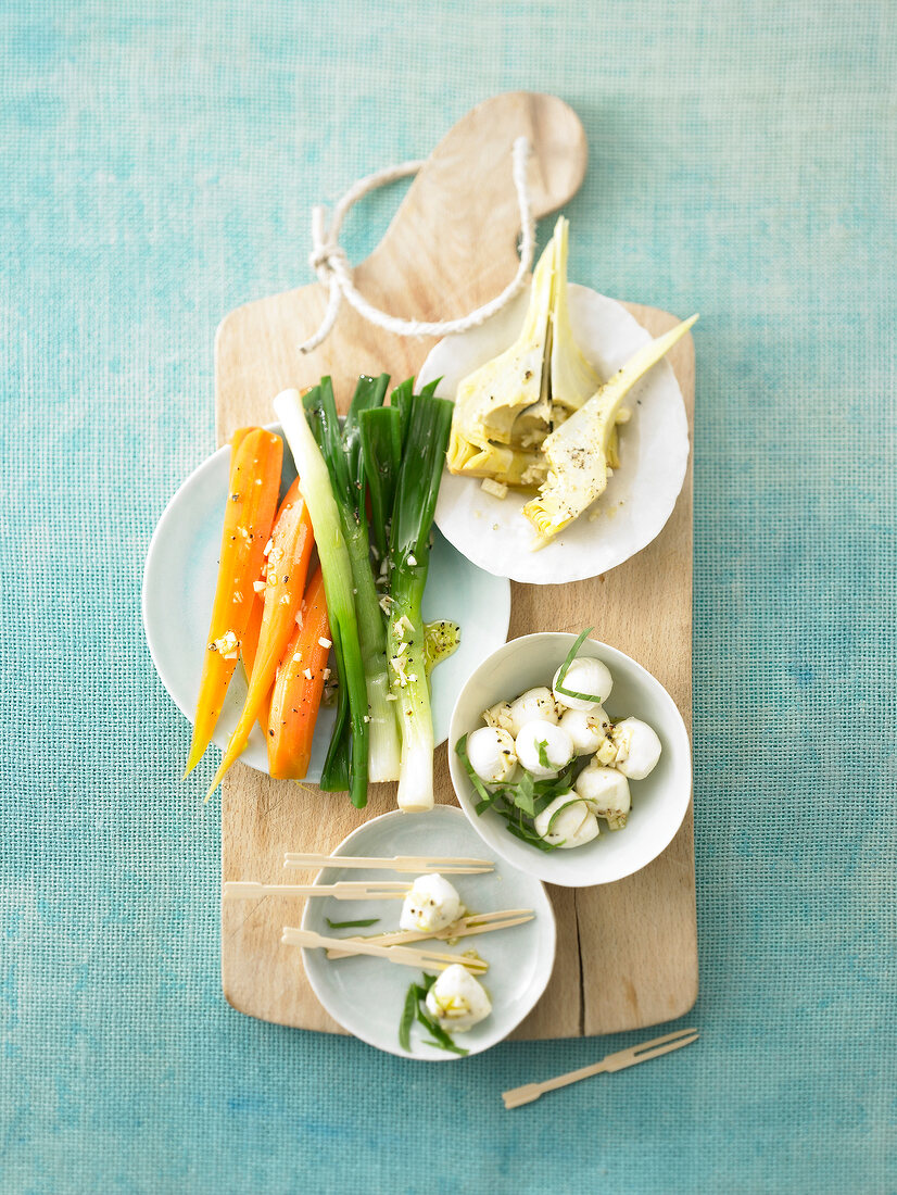 Carrots, spring, onions, artichoke and mozzarella on wood board, before meal