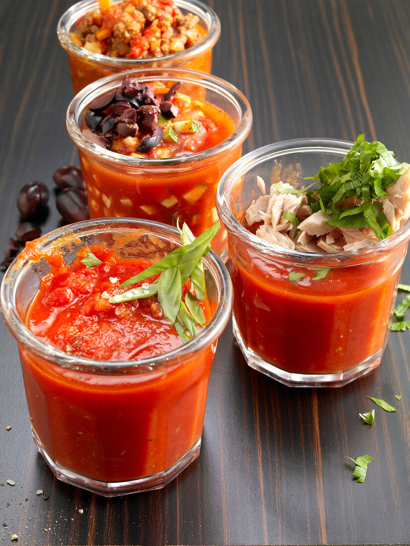 Close-up of four jars of tomato sauce with olives, tuna and herbs