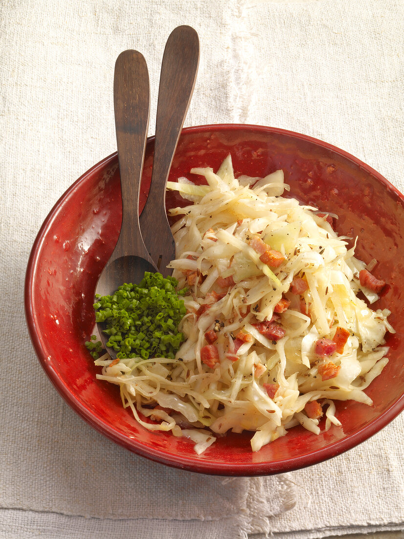 Salad with white cabbage, bacon, caraway seeds and chives in bowl