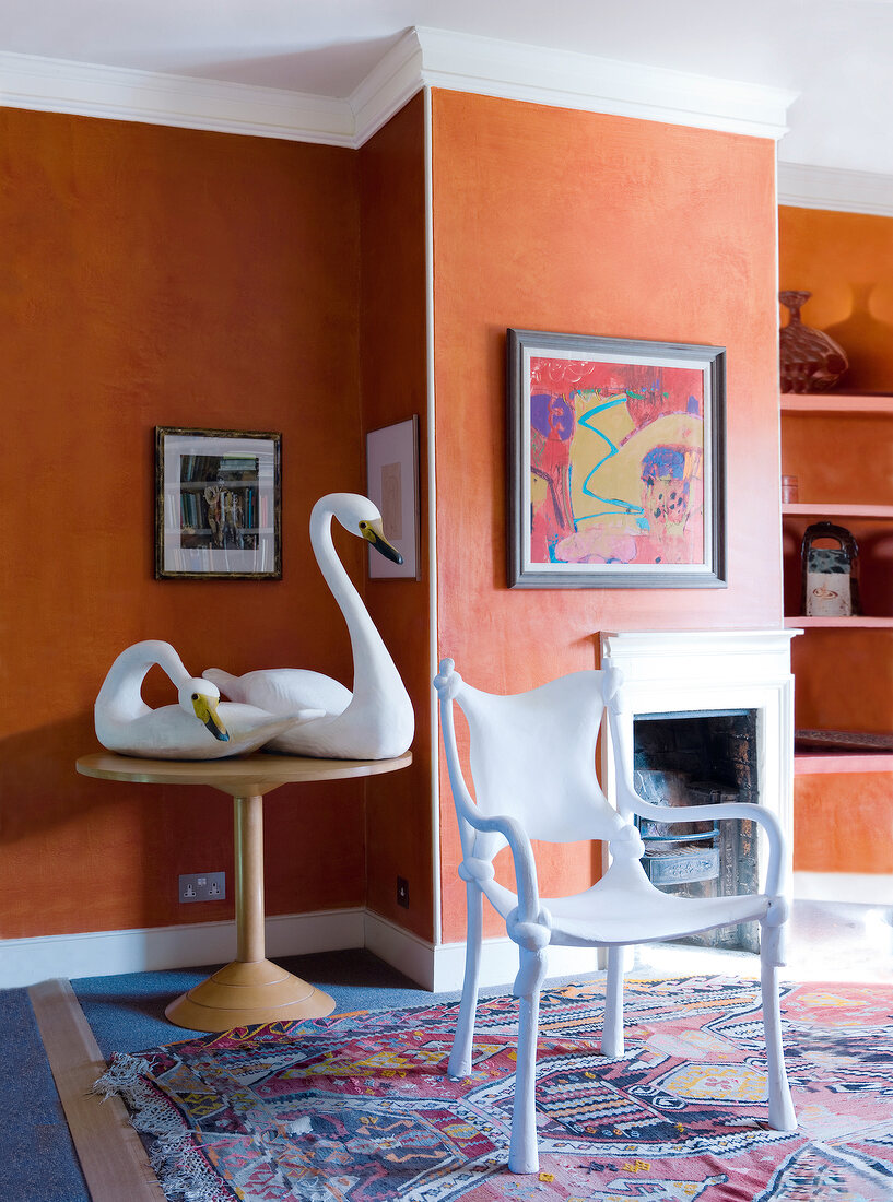 Swan statue on table with blanched oak chair against wall with paintings