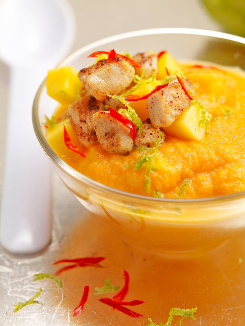 Close-up of carrot mousse garnished with mango and chicken in glass bowl