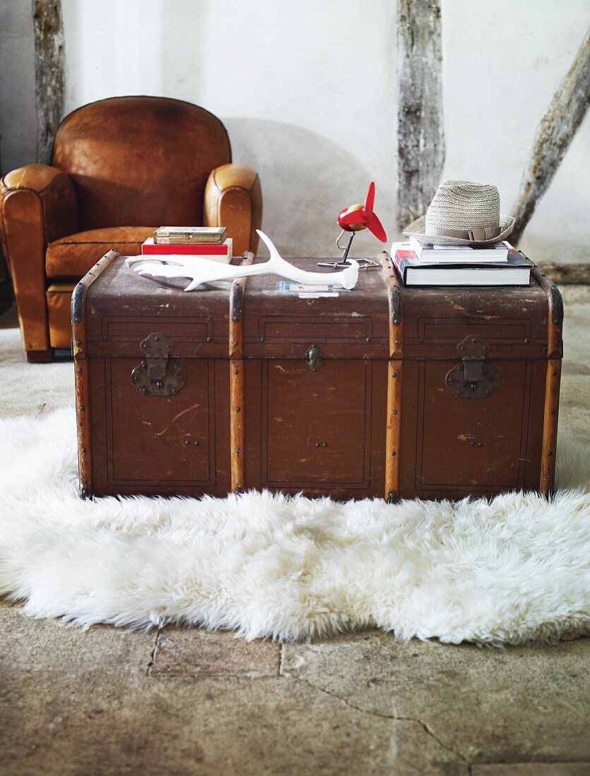 An old wooden chest being used as a coffee table on a white flock rug with a brown leather armchair in the background against a half-timbered wall