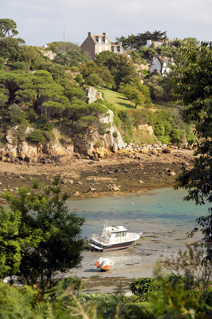 Boat in bay with rocks and trees in background near Paimpol, Brittany, France