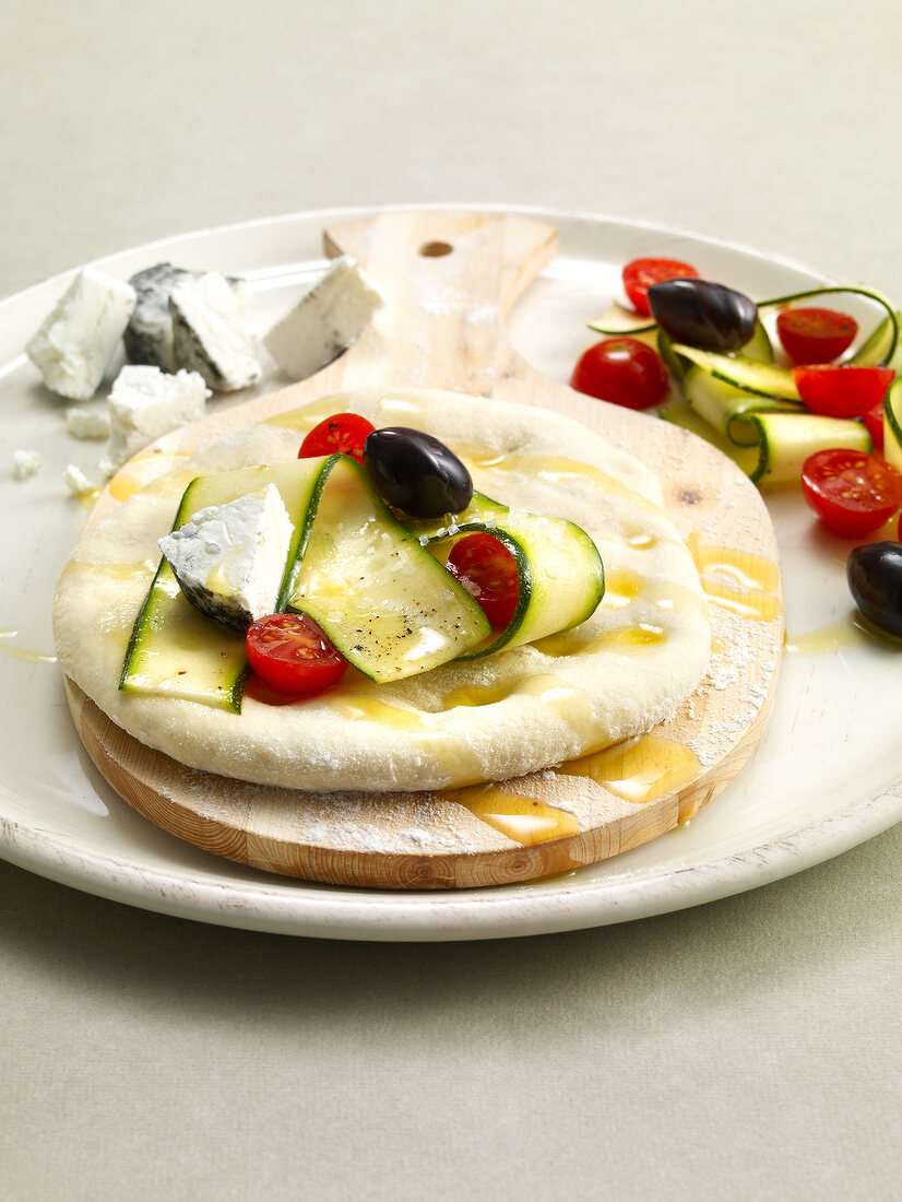 Raw pizza with tomatoes, goat cheese, olives and zucchini