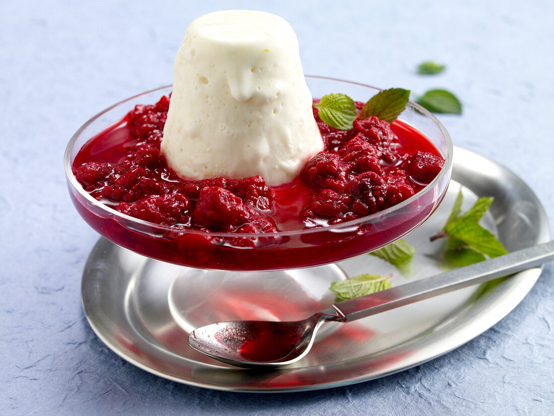 Goat cheese and honey ice cream with raspberry sauce and mint in glass cake stand