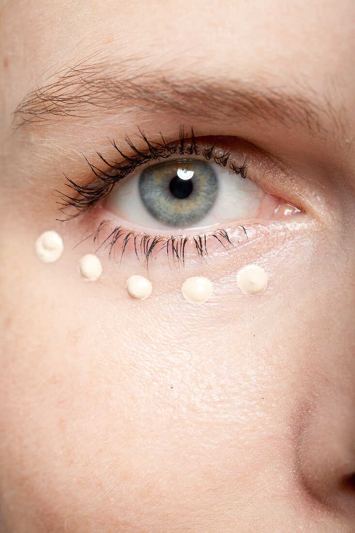 Close-up of gray eyed woman applying concealer under eye