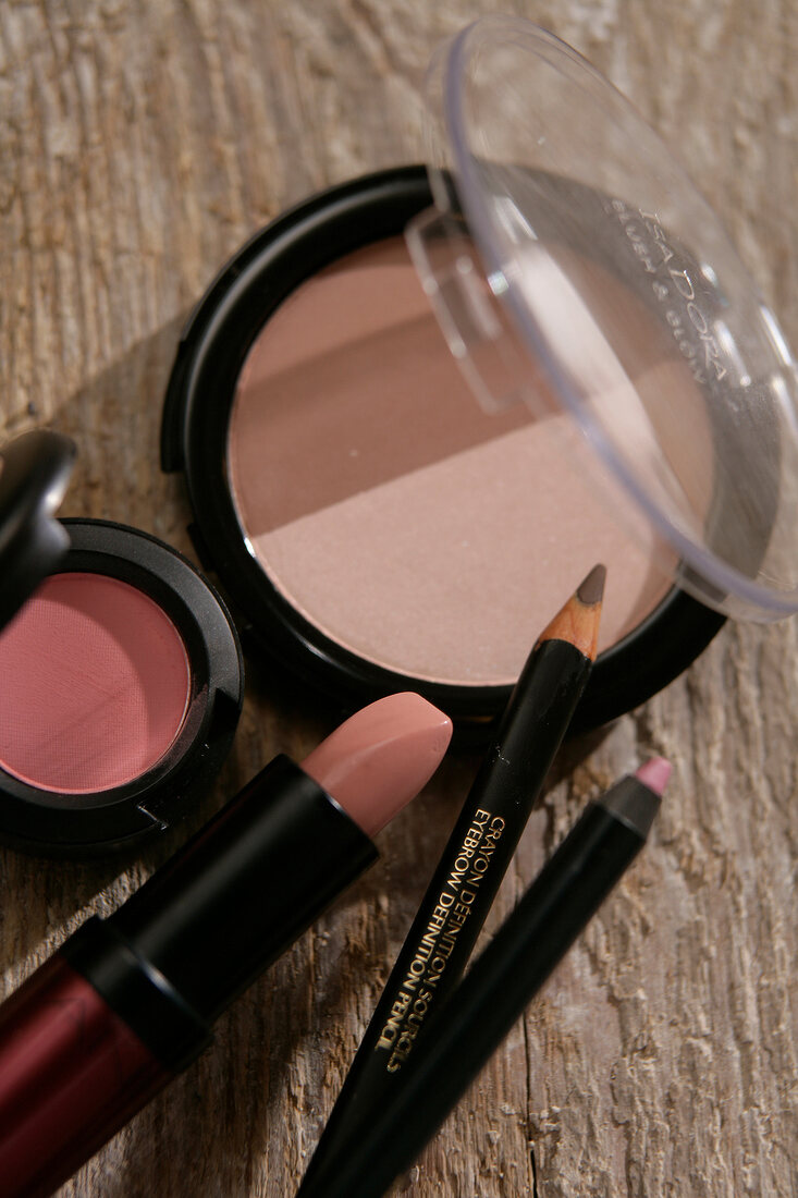 Close-up of pink eye shadow, blush, lip liner and lipstick on wooden surface