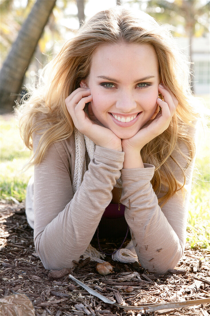 Portrait of beautiful blonde woman in top lying on front with head in hand and smiling