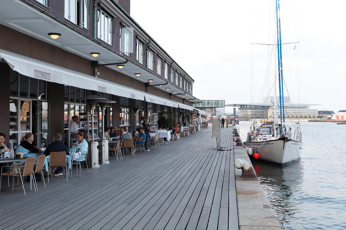 People sitting outside Costom House with boat near promenade, Copenhagen, Denmark