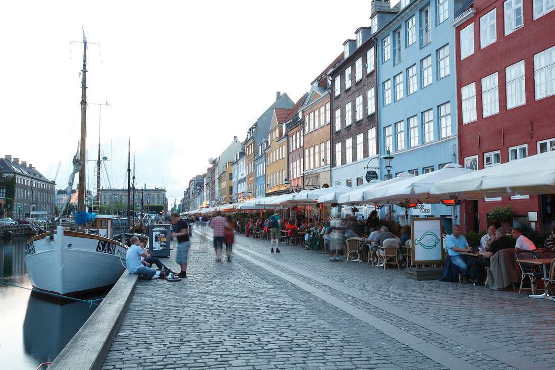 Kopenhagen: Nyhavn, Boote, Uferpro- menade, Häuser, Tische, Menschen.
