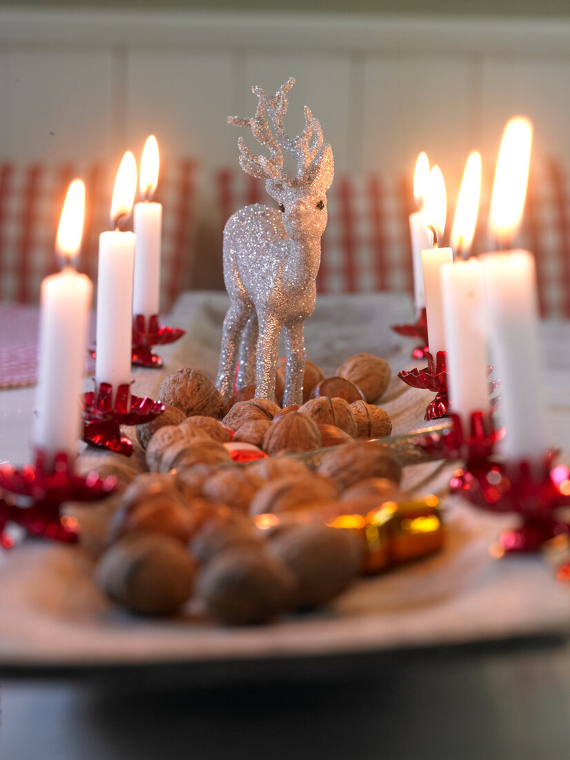 Close-up of wooden tray decorated with silver reindeer, lit candles and walnuts