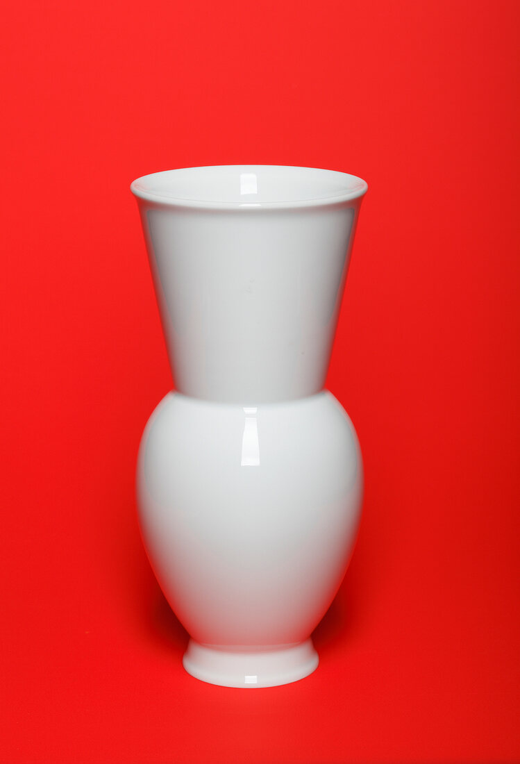 Close-up of white ceramic vase on red background