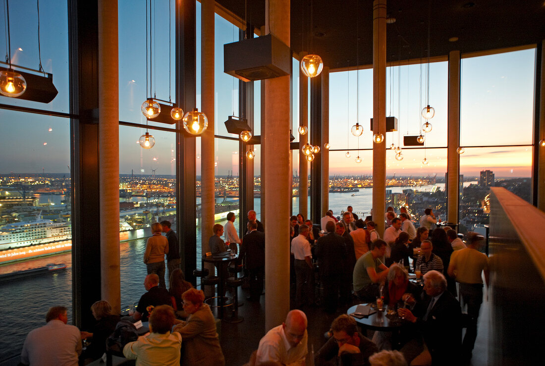People at restaurant looking at night view through panoramic window, Hamburg, Germany
