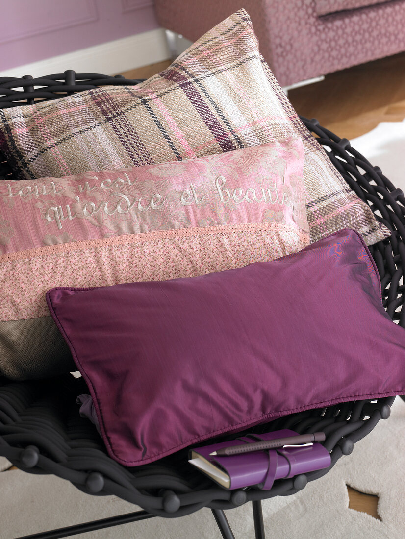 Close-up of purple and violet pillows with diary on wicker chair
