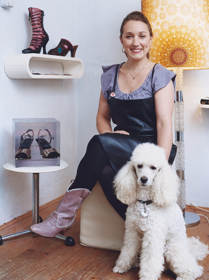 Portrait of woman sitting on chair with dog sitting on ground besides her, smiling