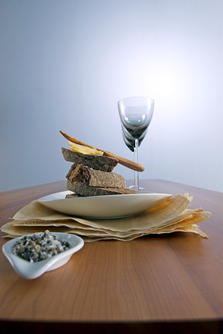 Plate with slices of bread and glasses on table