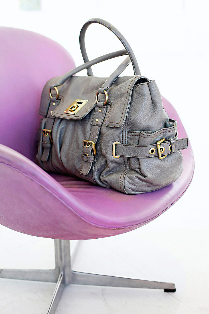 Close-up of gray leather bag on pink chair