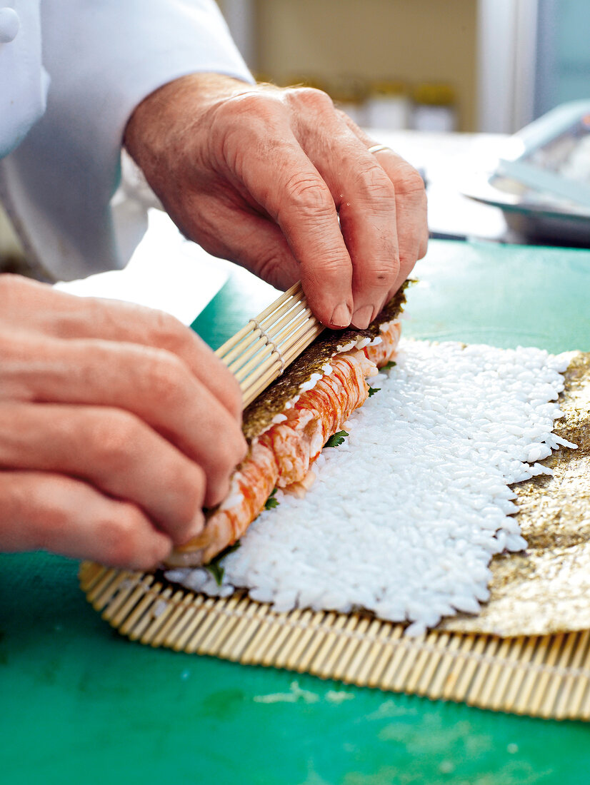 Close-up of man's hands wrapping langoustines in sushi roll on bamboo mat