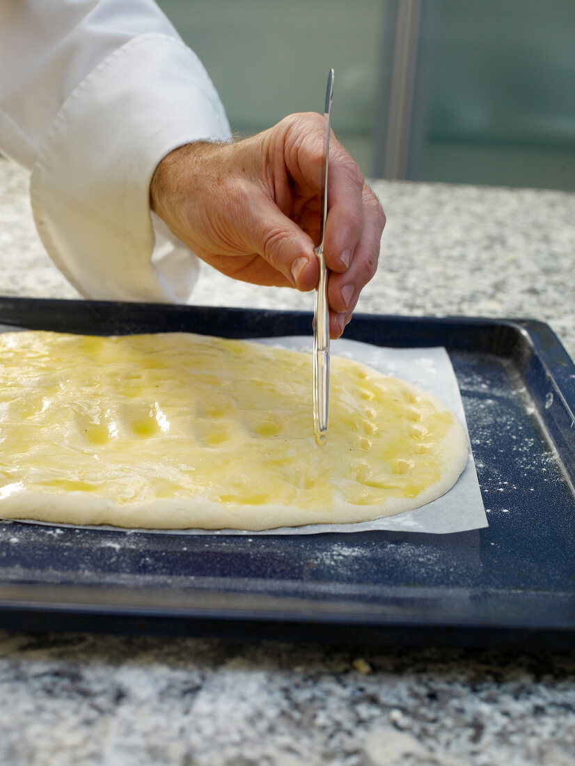 Close-up of man's hand making marks like troughs in bread dough for focaccia