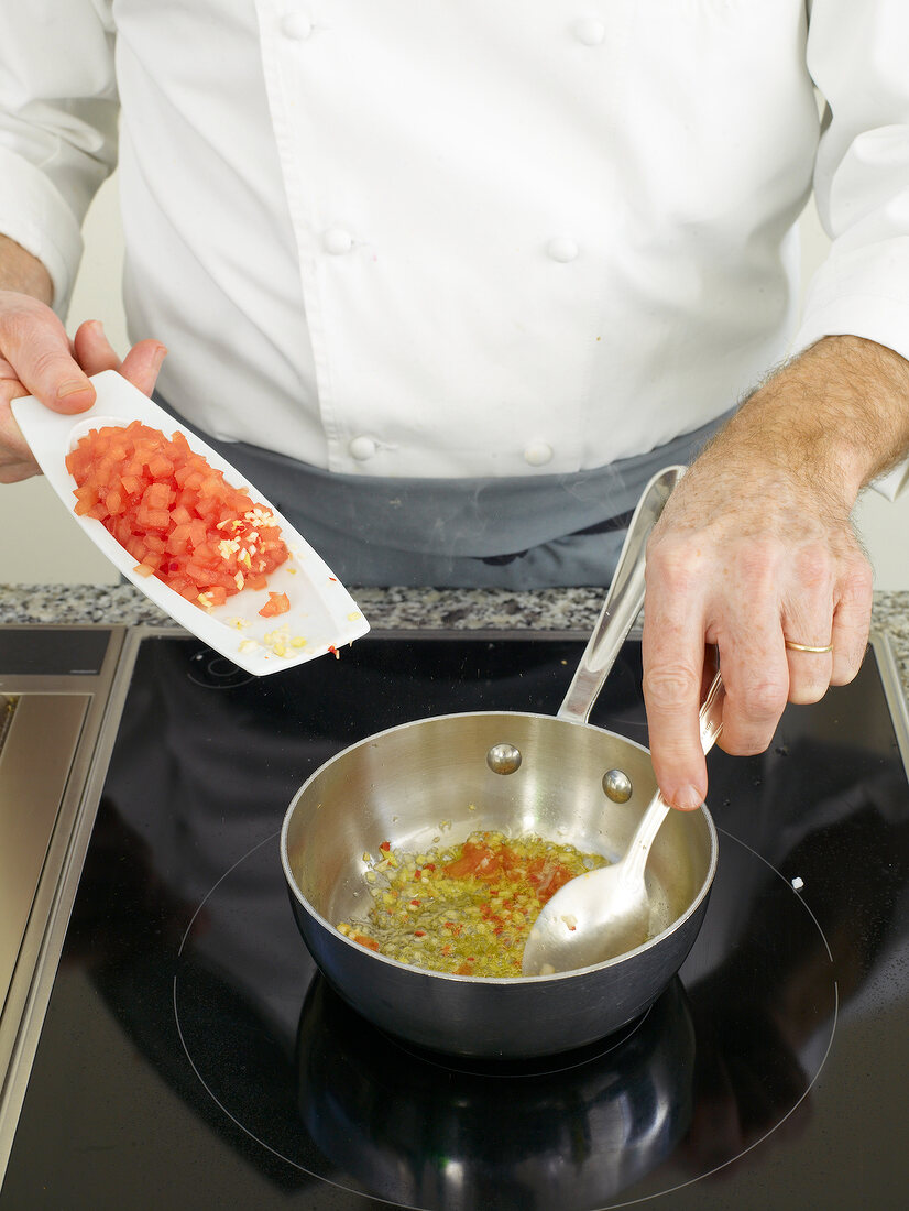 Man's hands adding diced tomatoes in saucepan