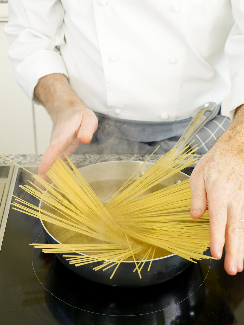 Man's hands adding spaghetti in pan for boiling it