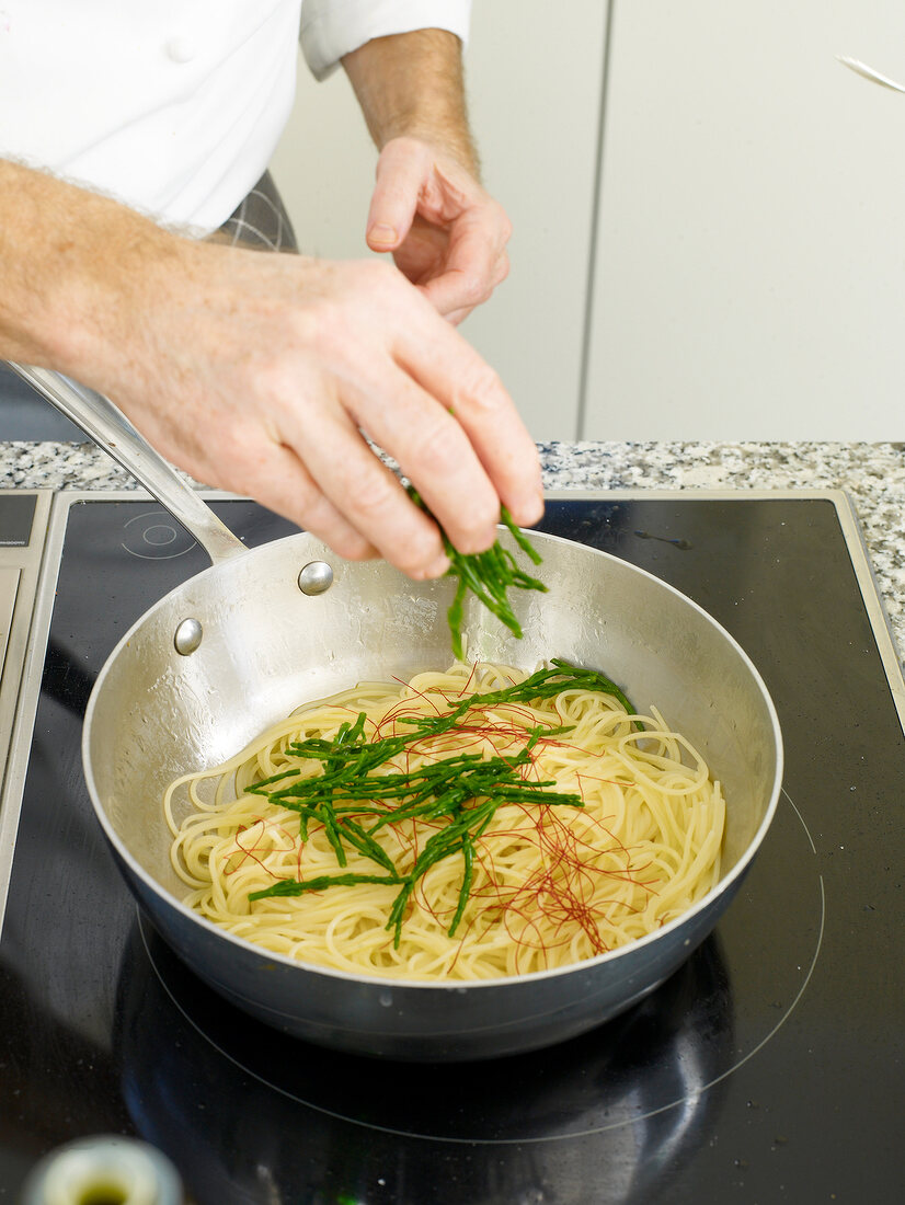 Close-up of man's hands adding salicorne in spaghetti with chilies