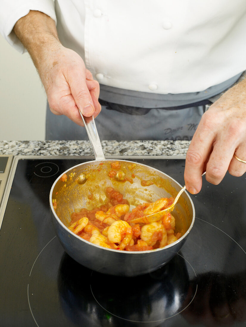 Close-up of man's hands mixing shrimps with tomato sauce in pan