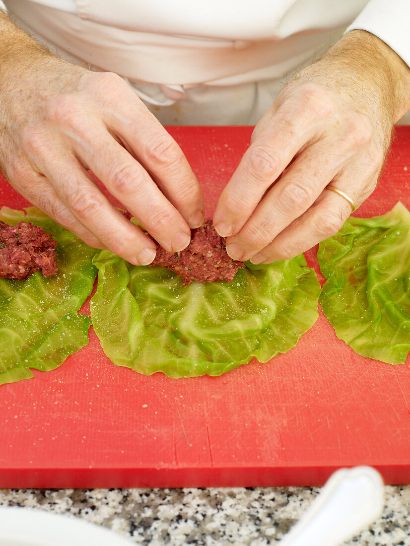 Close-up of man's hands stuffing ingredients on cabbage leaves