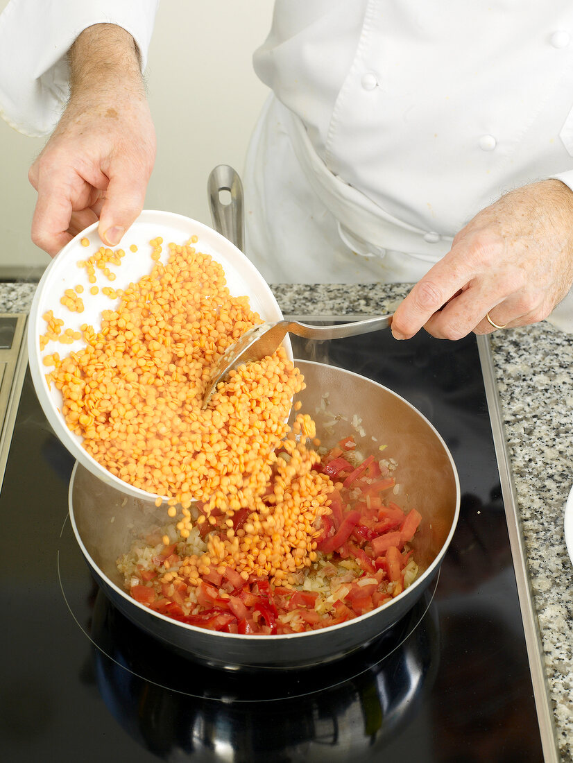 Close-up of man's hands adding ingredients with spoon in pan