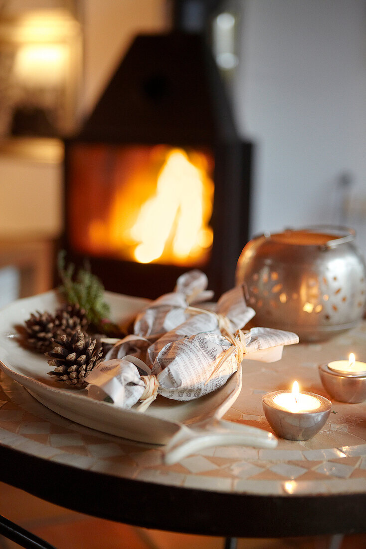 Pine cones, packed herbs and tea light on table in front of fireplace