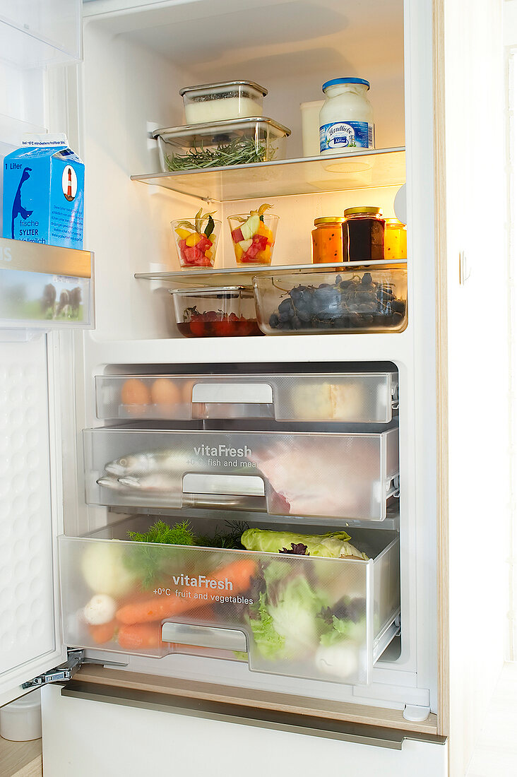 Refrigerator door open with various food on the shelves